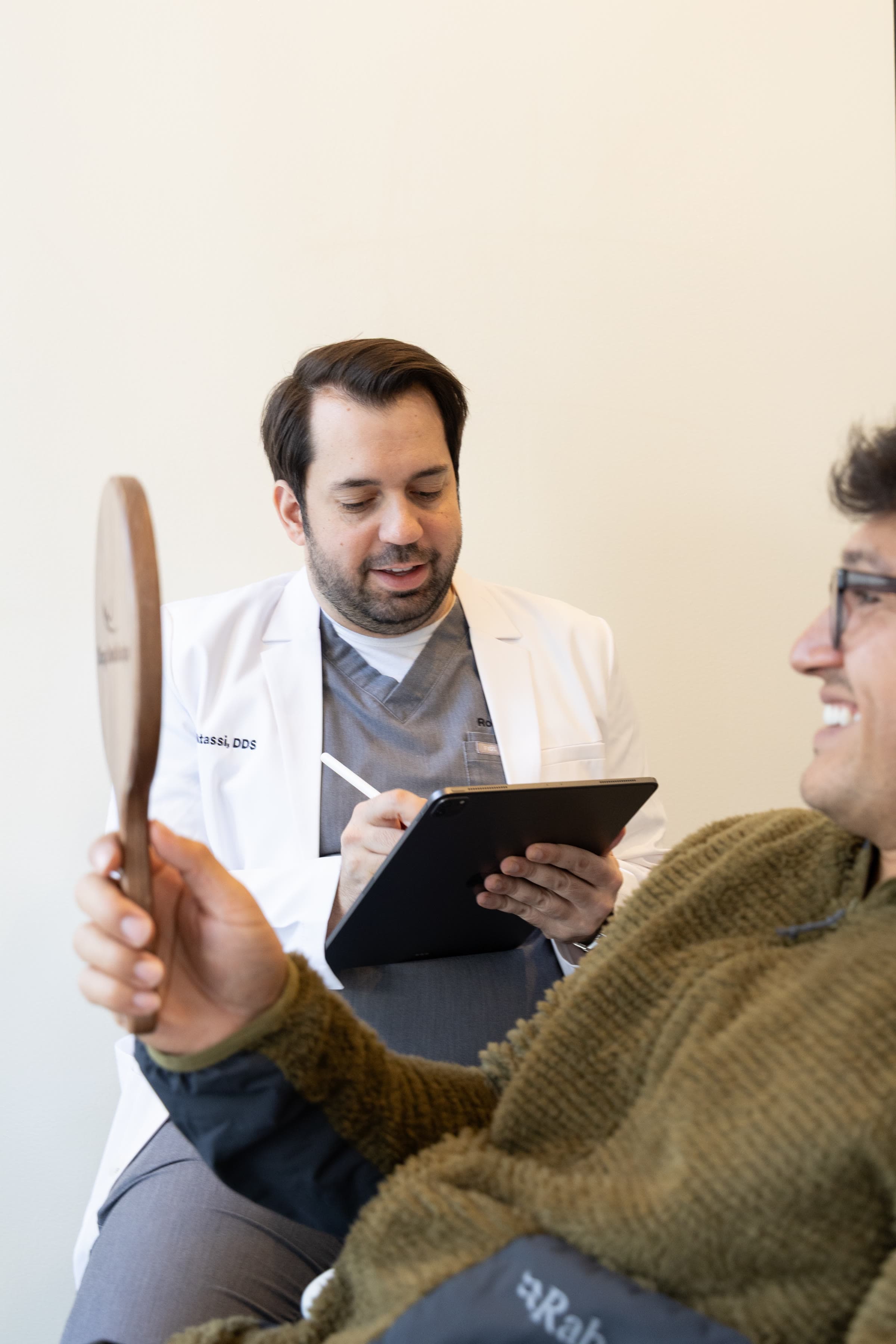 Dr. Atassi sketching a smile design on a tablet while the patient holds a mirror